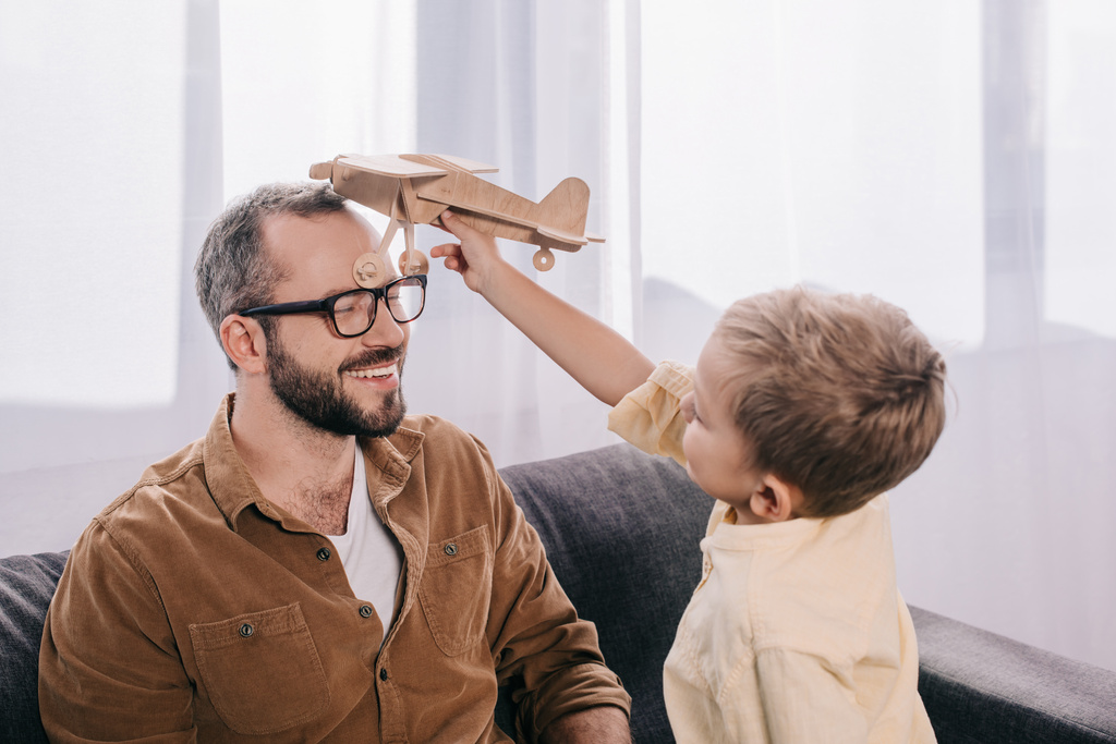 счастливые отец и сын играют дома с деревянным игрушечным самолетом
 - Фото, изображение