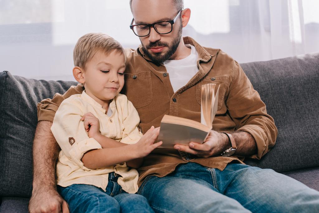otec a syn sedí na gauči a čtení knihy dohromady - Fotografie, Obrázek