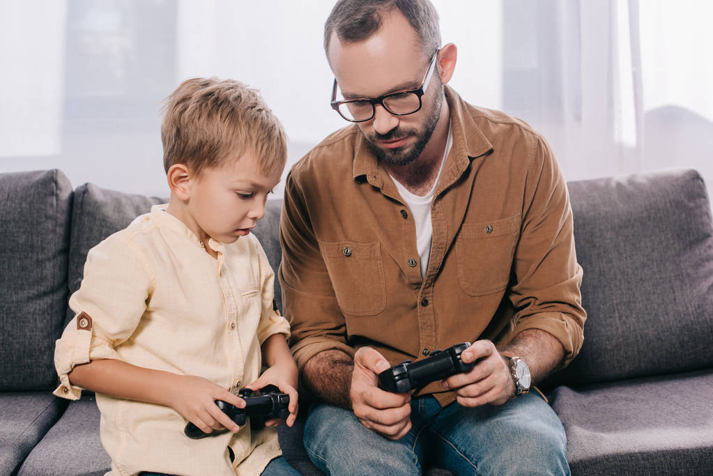 padre y lindo hijo pequeño jugando juntos con joysticks en casa
 - Foto, Imagen