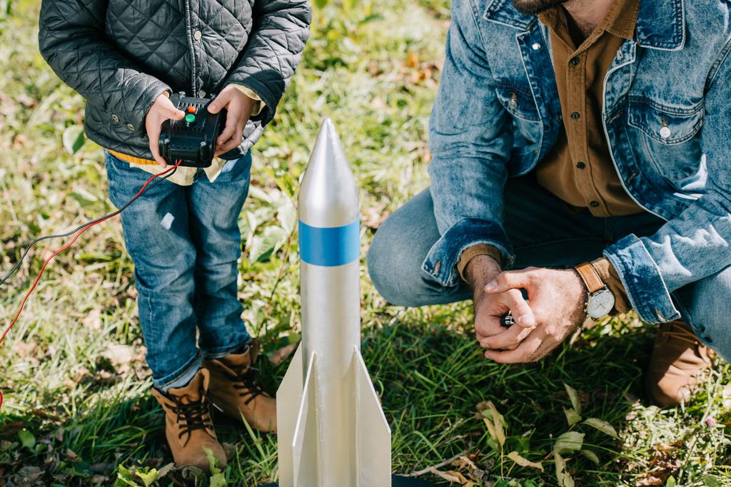 обрезанный снимок отца и маленького сына, запускающих модель ракеты на открытом воздухе
 - Фото, изображение