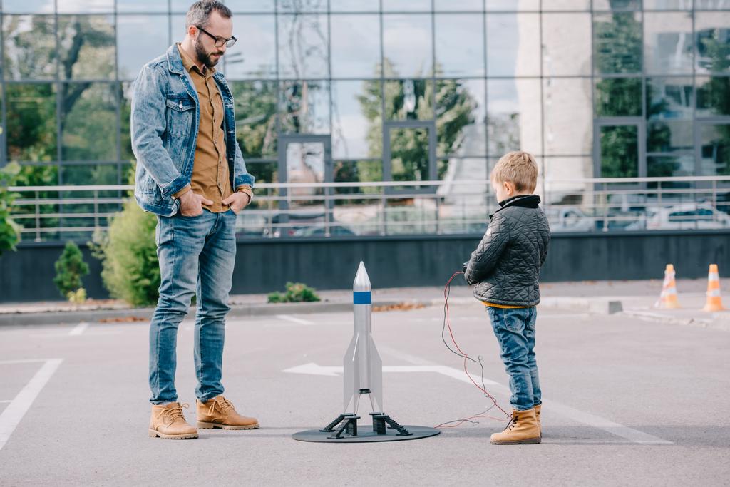 Isä katselee pieni poika käynnistää malli raketti ulkona
 - Valokuva, kuva