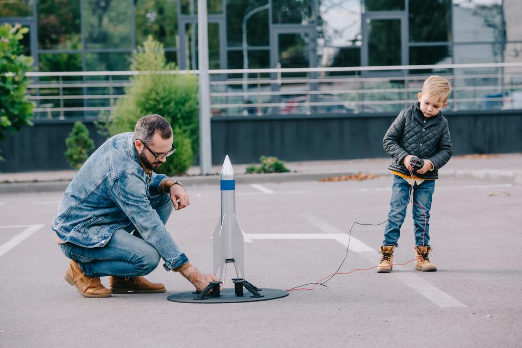 pai e pequeno filho brincando com modelo de foguete ao ar livre
  - Foto, Imagem