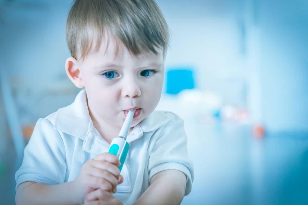 Carino piccolo ragazzo biondo dagli occhi azzurri con una polo bianca che si lava i denti con uno spazzolino da denti
 - Foto, immagini