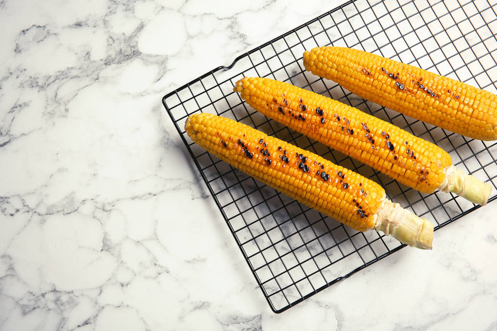 Cooling rack with grilled corn cobs on marble background, top view. Space for text - Photo, Image