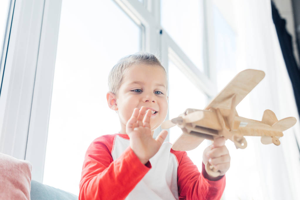smiling child playing with toy wooden plane at home - Photo, Image