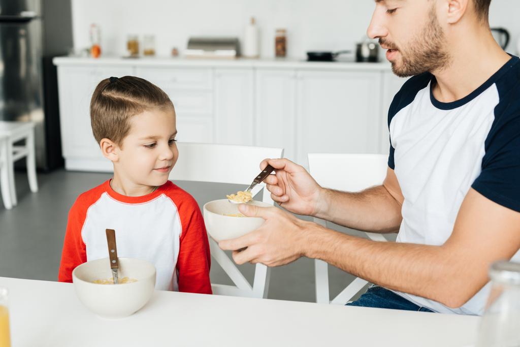 Vater füttert Sohn beim gemeinsamen Frühstück in Küche - Foto, Bild