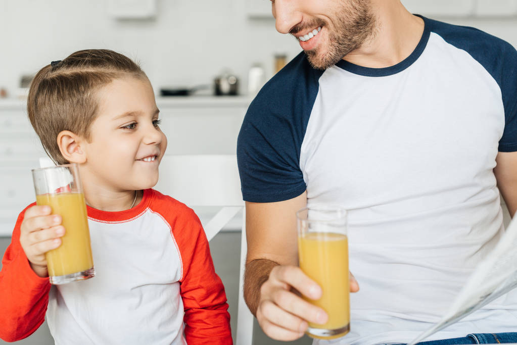 részleges kilátás Atya és boldog fiú pohár gyümölcslé reggeli közben otthon a konyhában - Fotó, kép