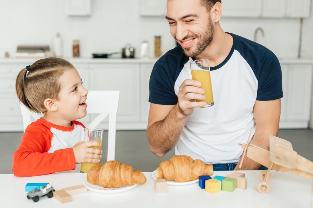 przystojny młody ojciec i syn o śniadanie z rogalikami i sok pomarańczowy razem w domu - Zdjęcie, obraz