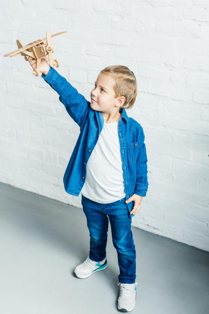 чарівна маленька дитина грає з дерев'яним іграшковим літаком перед білою цегляною стіною
 - Фото, зображення