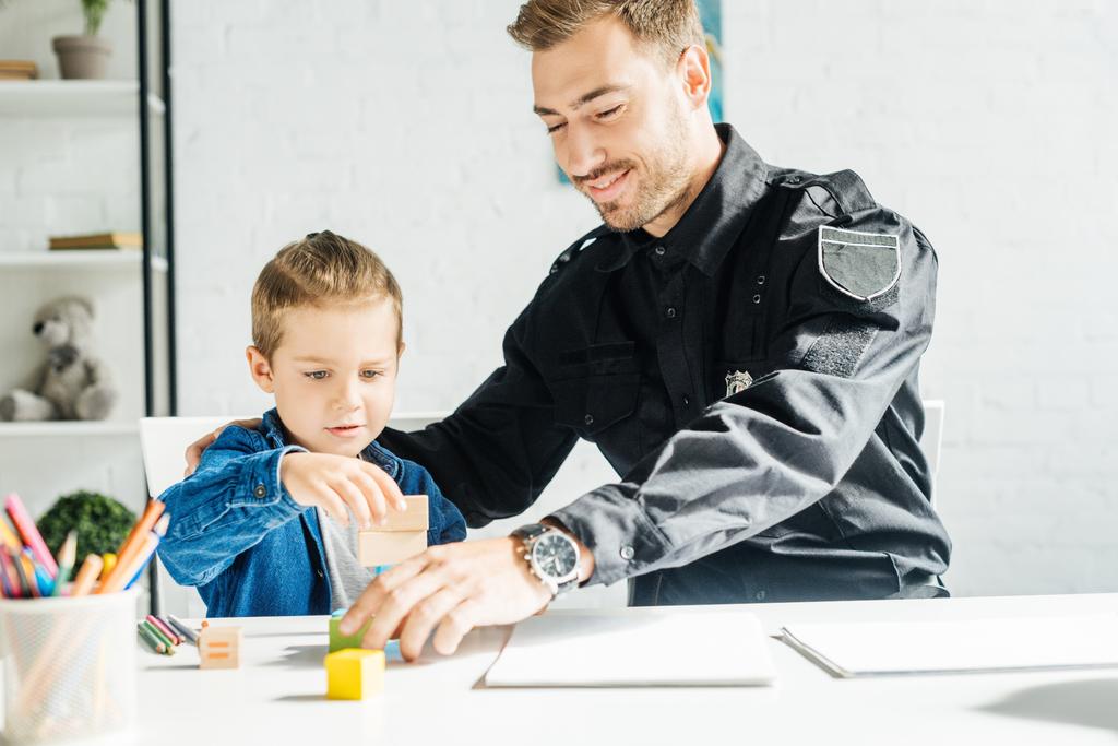 χαρούμενος νεαρός πατέρας στην αστυνομία ομοιόμορφη και γιο να παίζουν μαζί στο σπίτι - Φωτογραφία, εικόνα