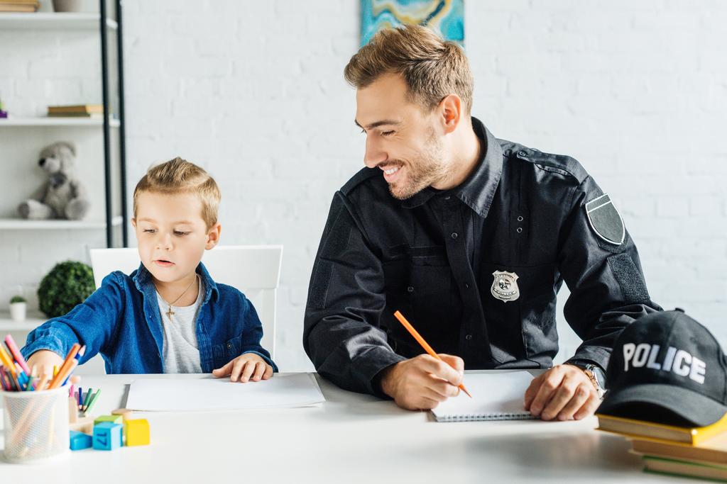 szczęśliwy ojciec młodych w jednolitego policji i jego synek rysunek razem w domu - Zdjęcie, obraz