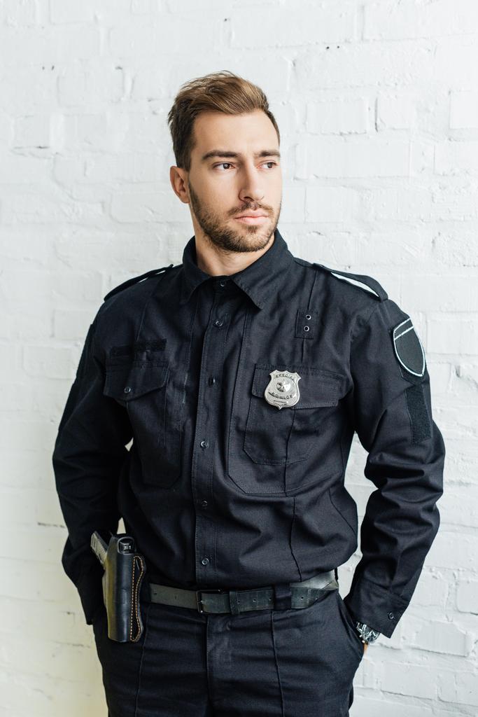 portrait of handsome young policeman in front of white brick wall - Photo, Image