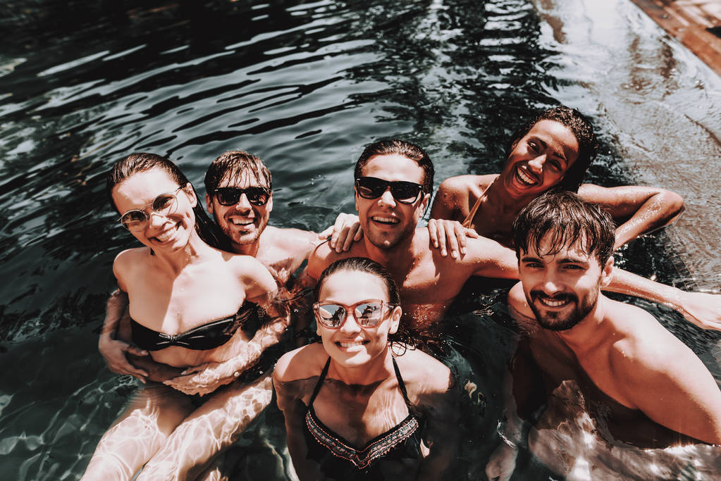 Jóvenes amigos felices en la piscina al aire libre. Grupo de jóvenes sonrientes que llevan gafas de sol divirtiéndose juntos nadando en la piscina del hotel. Amigos Enoying Pool Party. Concepto de vacaciones de verano
 - Foto, Imagen