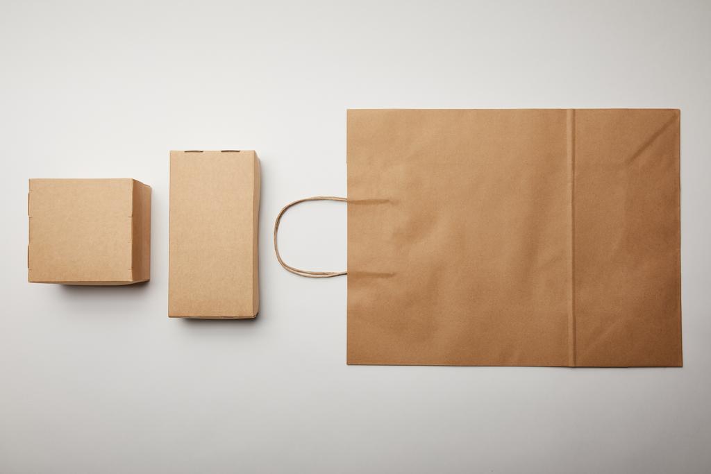vista elevada da vista arranjada de caixas de papelão e saco de papel de entrega de alimentos na superfície branca, conceito minimalista
  - Foto, Imagem