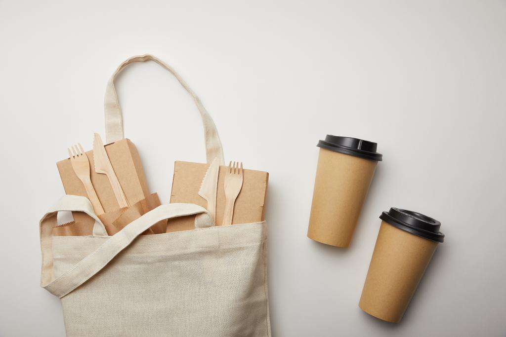 υπερυψωμένη θέα βαμβακερή τσάντα με δύο κούπες καφέ μίας χρήσης κιβώτια τροφίμων σε λευκή επιφάνεια - Φωτογραφία, εικόνα