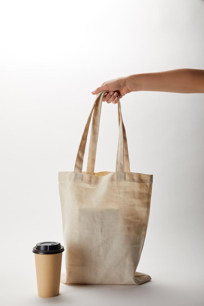 Μερική άποψη της γυναίκας κρατώντας βαμβακερή τσάντα με τρόφιμα παράδοσης και χαρτί κούπα καφέ κοντά σε λευκό - Φωτογραφία, εικόνα