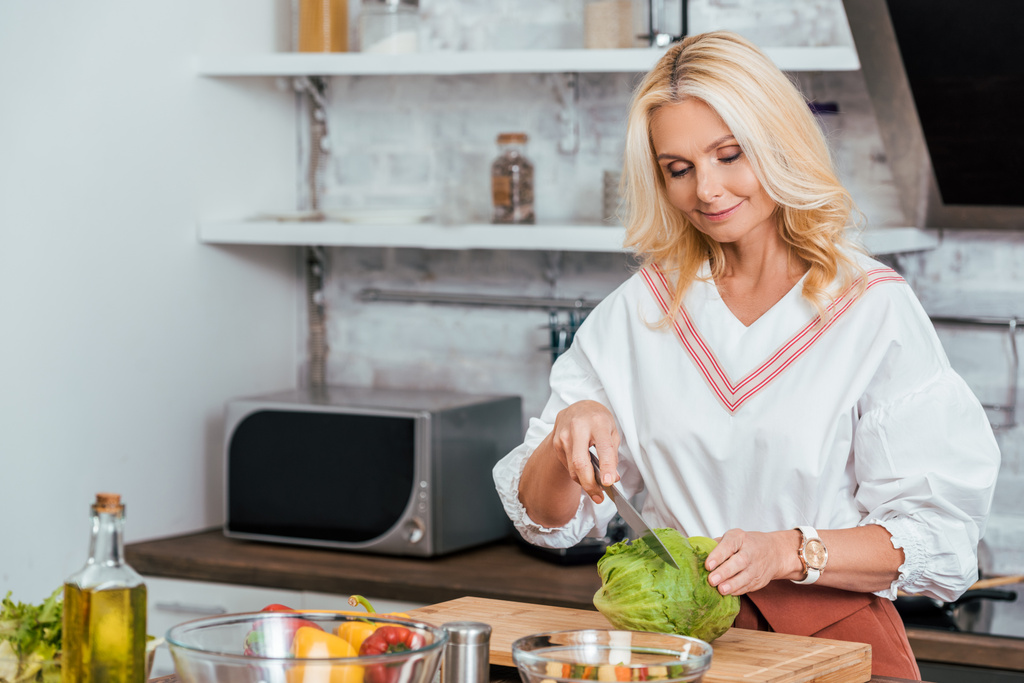 adult blonde woman preparing salad for dinner and cutting cabbage at home - Photo, Image