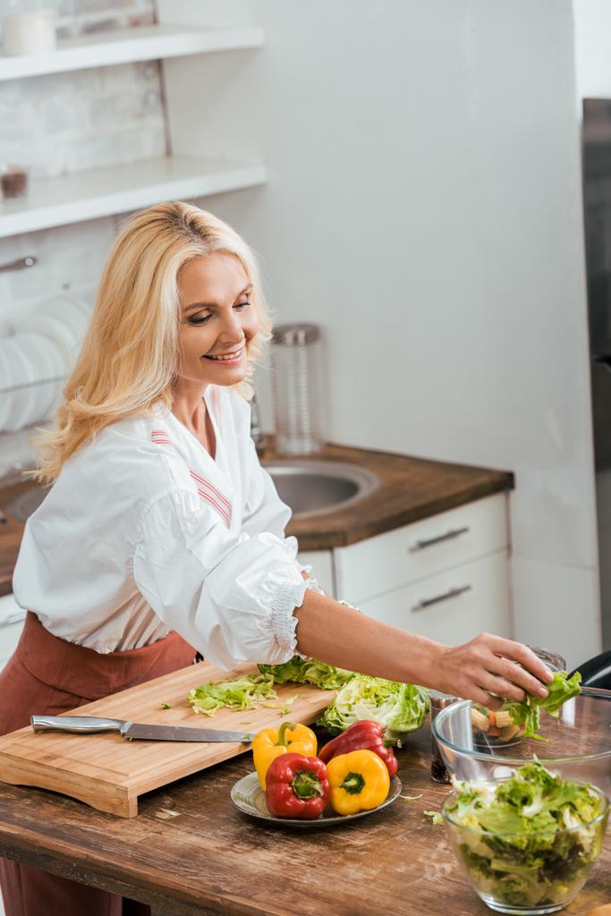 attraktive Frau bereitet Salat für das Abendessen zu und legt Zutaten in Schüssel zu Hause - Foto, Bild