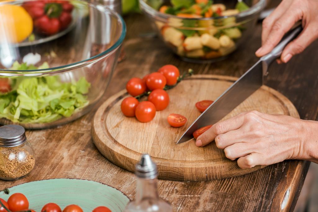 przycięty obraz kobiety przygotowanie Sałatka na kolację i cięcia Pomidory czereśniowe w domu - Zdjęcie, obraz