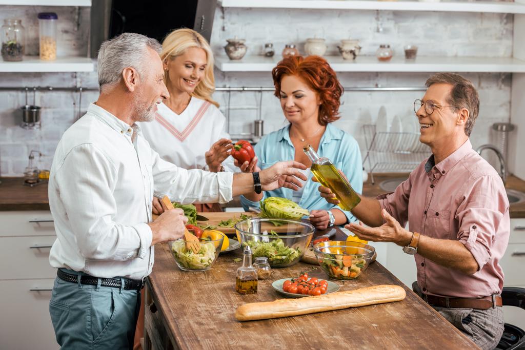 mature male and female friends preparing salad for dinner at home - Photo, Image