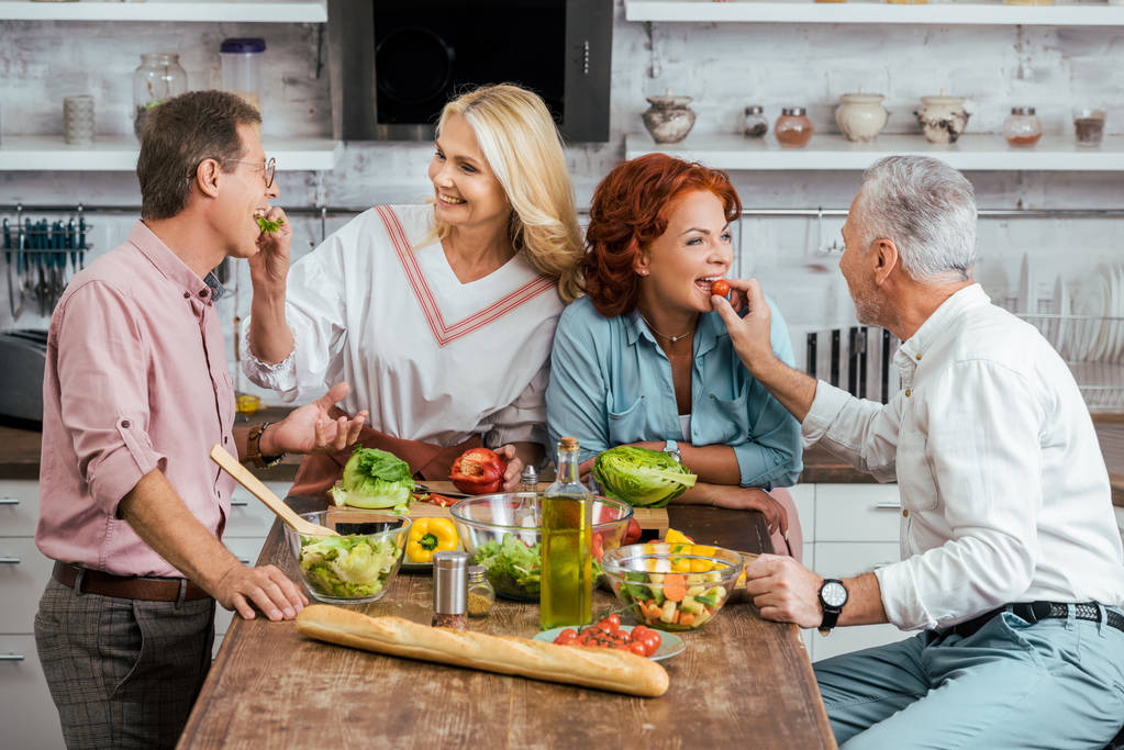 couples d'âge mûr heureux se nourrissant pendant la préparation de la salade pour le dîner à la maison
 - Photo, image