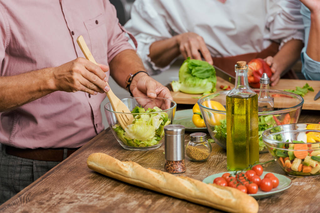 обрезанный образ зрелых друзей, готовящих салат к ужину вместе дома
 - Фото, изображение