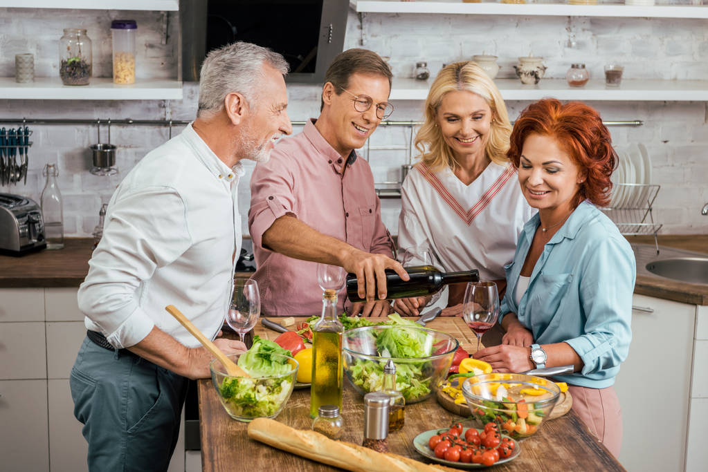 knappe man gieten wijn aan gelukkig oude vrienden tijdens het diner thuis - Foto, afbeelding