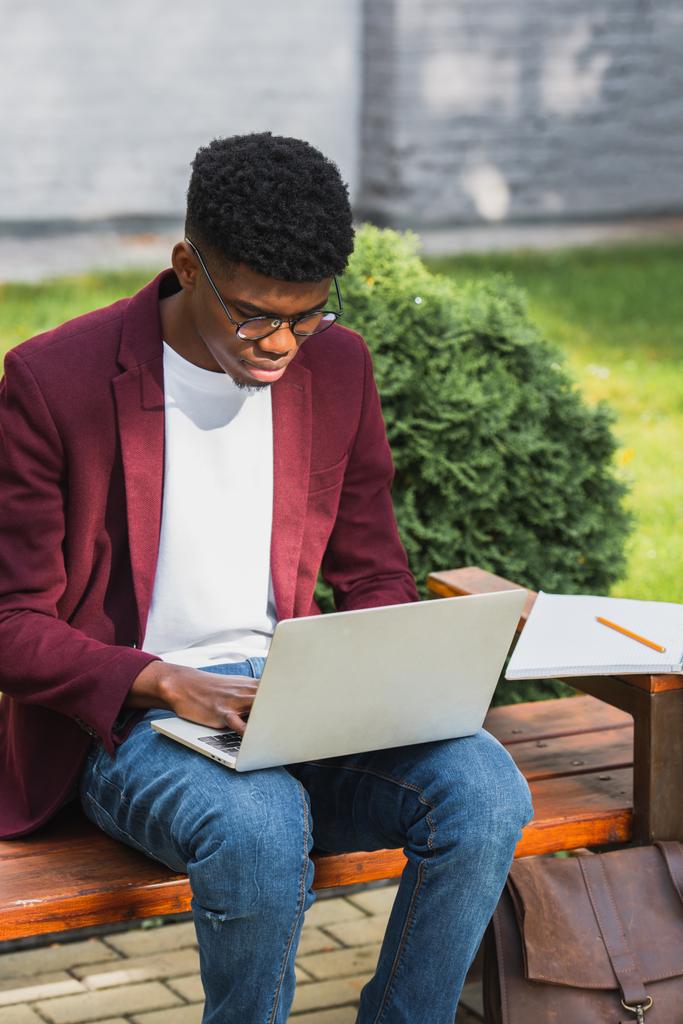 Afrikkalainen amerikkalainen nuori freelancer käyttäen kannettavaa tietokonetta penkillä
 - Valokuva, kuva