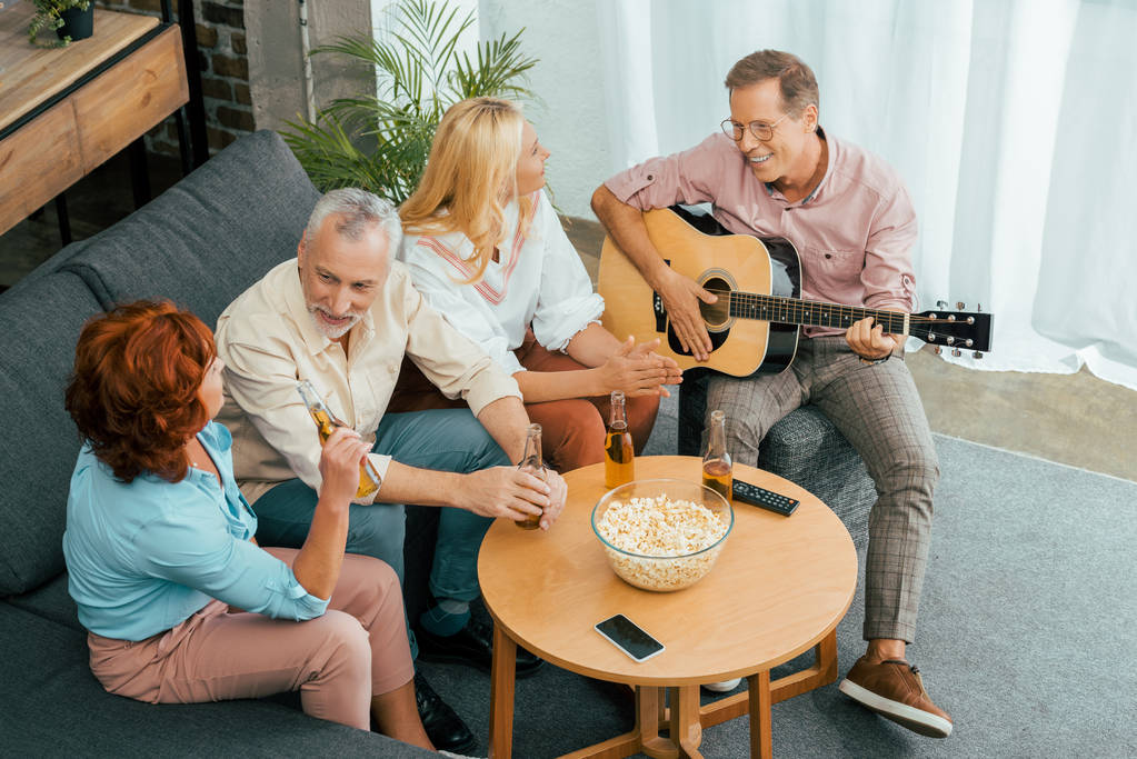 high angle view of happy mature friends spending time with guitar and beer at home  - Photo, Image