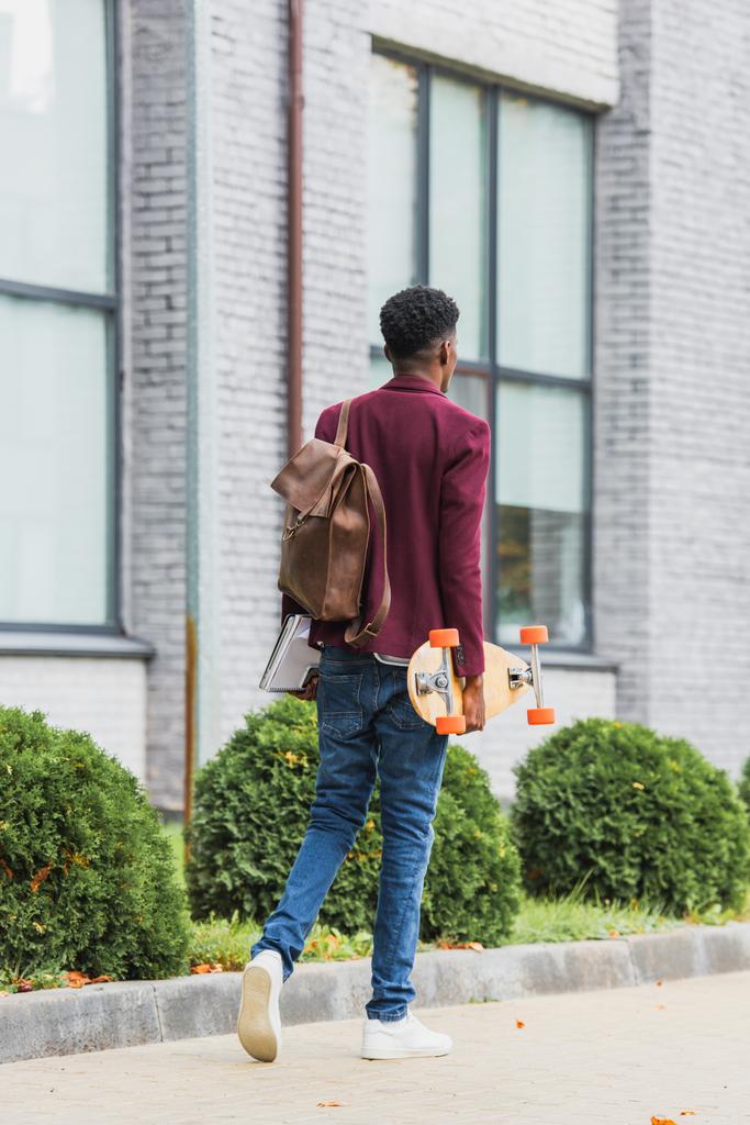 vue arrière du jeune étudiant avec sac à dos et planche à roulettes marchant dans la rue
 - Photo, image