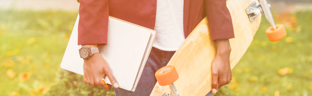 обрізаний широкий знімок стильного студента з блокнотами та скейтбордом, що стоїть на вулиці
 - Фото, зображення