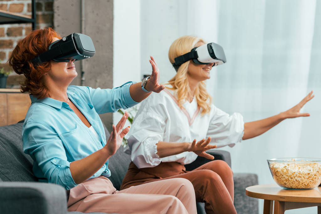 Gelukkig rijpe vrouwen zittend op de Bank en het gebruik van virtuele realiteit headsets  - Foto, afbeelding