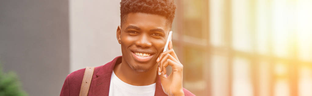 brede afgezwakt schot van glimlachen jonge man praten via de telefoon en de camera kijken op straat - Foto, afbeelding