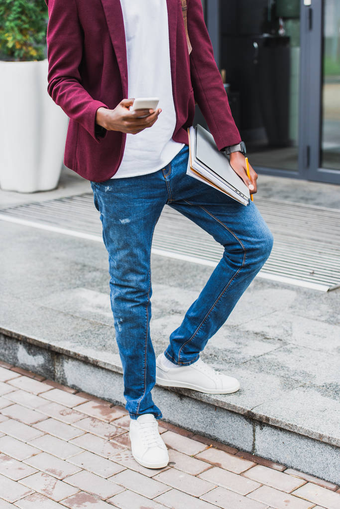 cropped shot of stylish student with notebooks and smartphone standing on street - Photo, Image