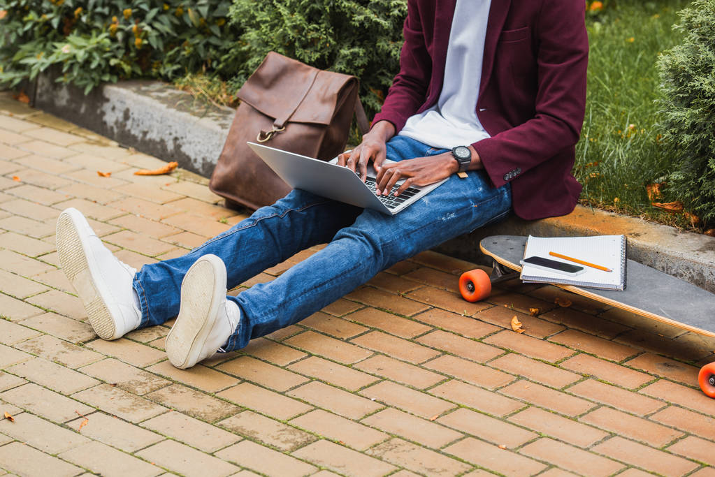 recortado disparo de freelancer usando portátil mientras está sentado en la acera en la calle
 - Foto, Imagen