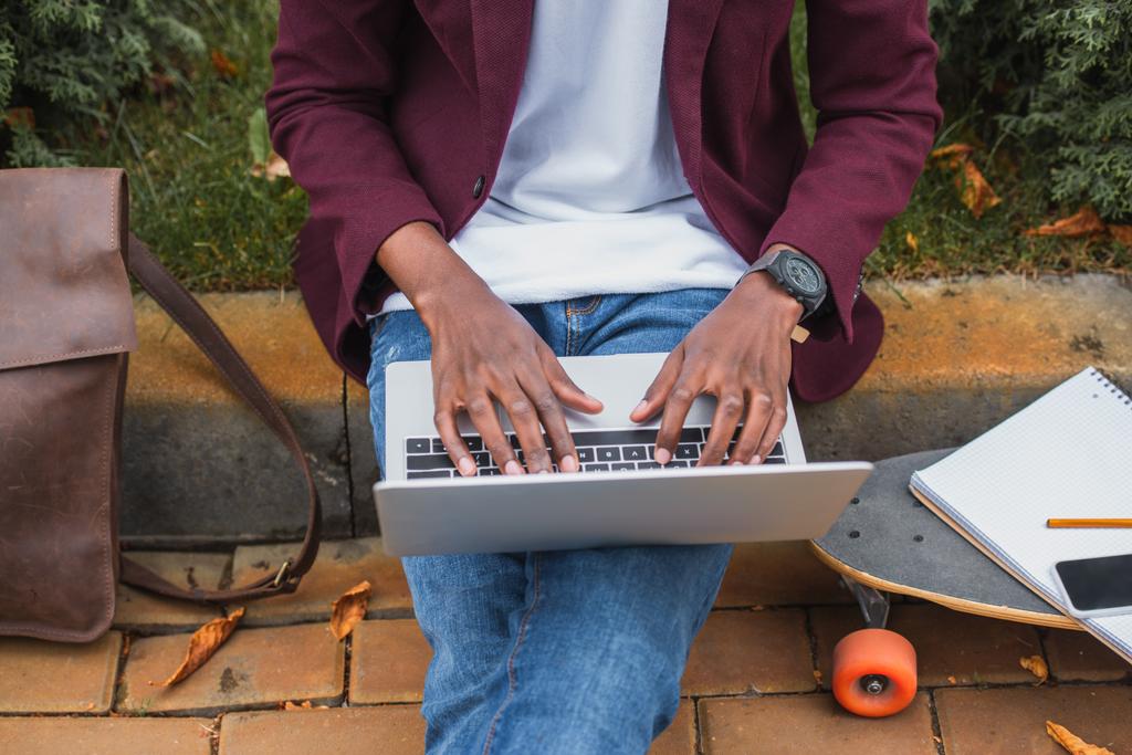 vágott lövés a fiatal szabadúszó használ laptop ülve a járdára utca - Fotó, kép