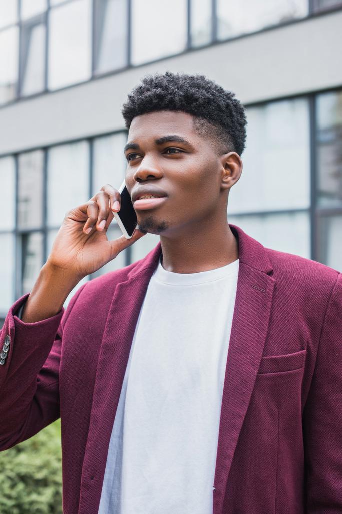 привлекательный молодой человек разговаривает по телефону на улице и смотрит в сторону
 - Фото, изображение