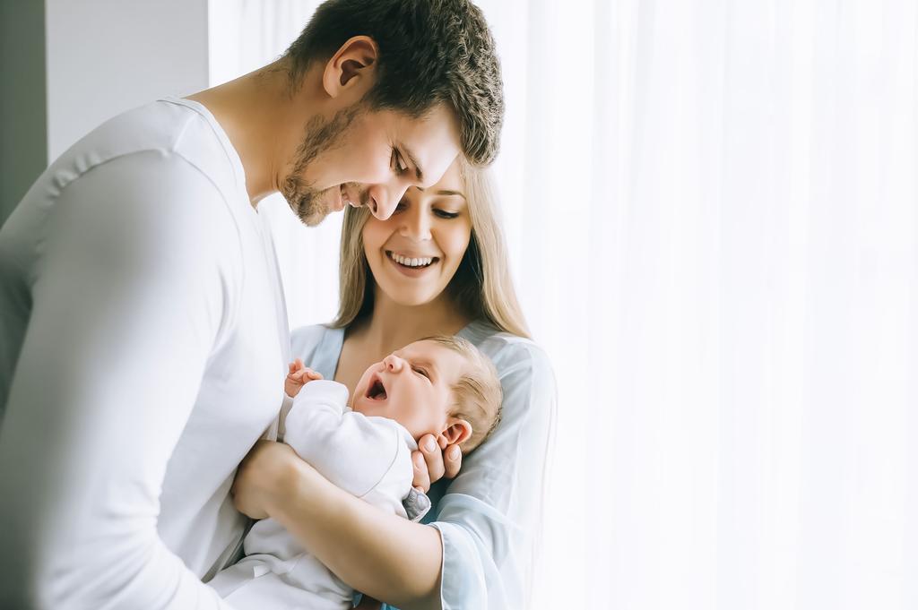 smiling family carrying little baby boy in front of curtains at home - Photo, Image