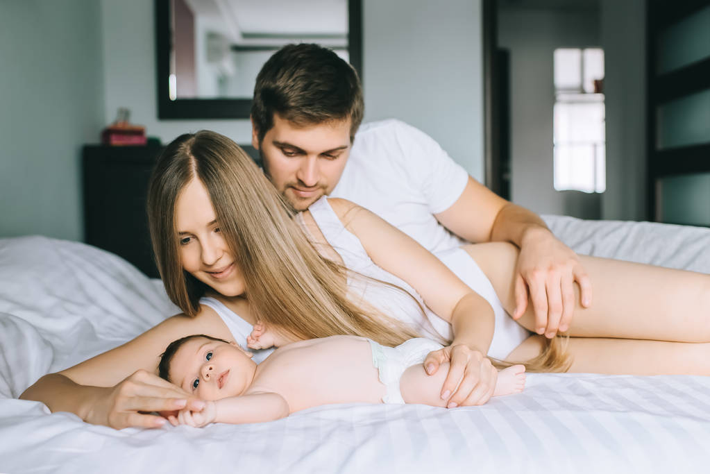 επιλεκτική εστίαση του ευτυχισμένη οικογένεια στην τοποθέτηση με αξιολάτρευτο μικρό γιο το μωρό στο κρεβάτι στο σπίτι - Φωτογραφία, εικόνα
