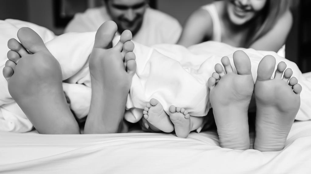 black and white picture of legs of family with infant son under blanket in bed at home - Photo, Image