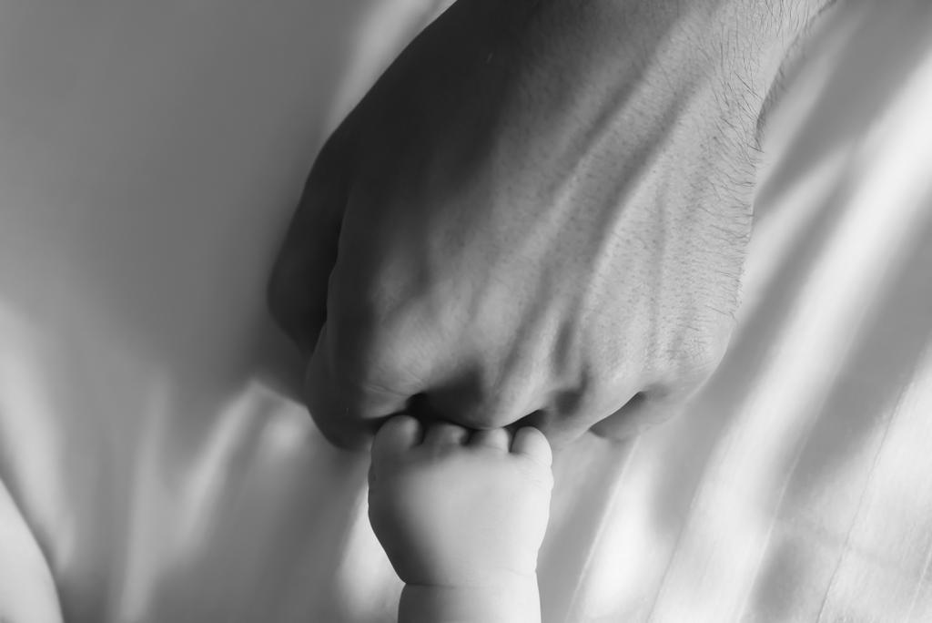 black and white picture of hands of man and infant son in bed  - Photo, Image