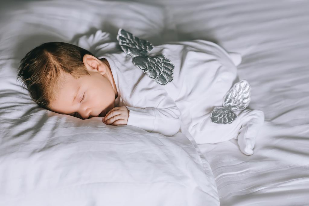 чарівний маленький хлопчик в костюмі з крилами спить в ліжку вдома
 - Фото, зображення