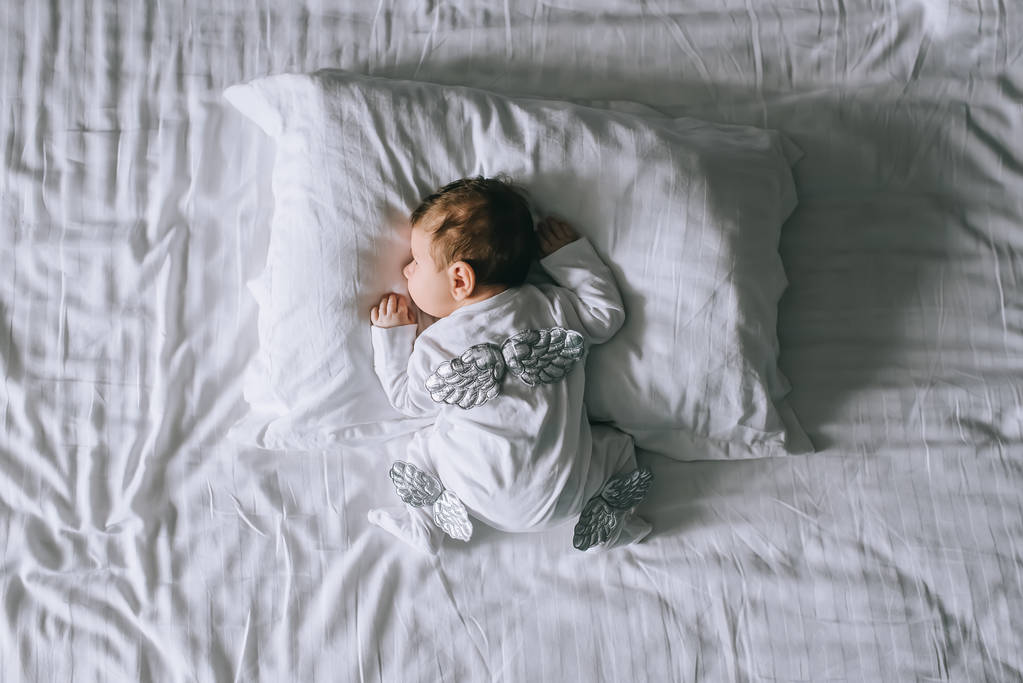 vista aerea del bambino in costume con le ali distese a letto a casa
 - Foto, immagini