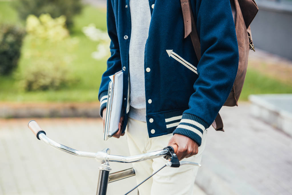 rajattu näkymä mies opiskelija paperit kannettava tietokone ja polkupyörän kadulla
 - Valokuva, kuva