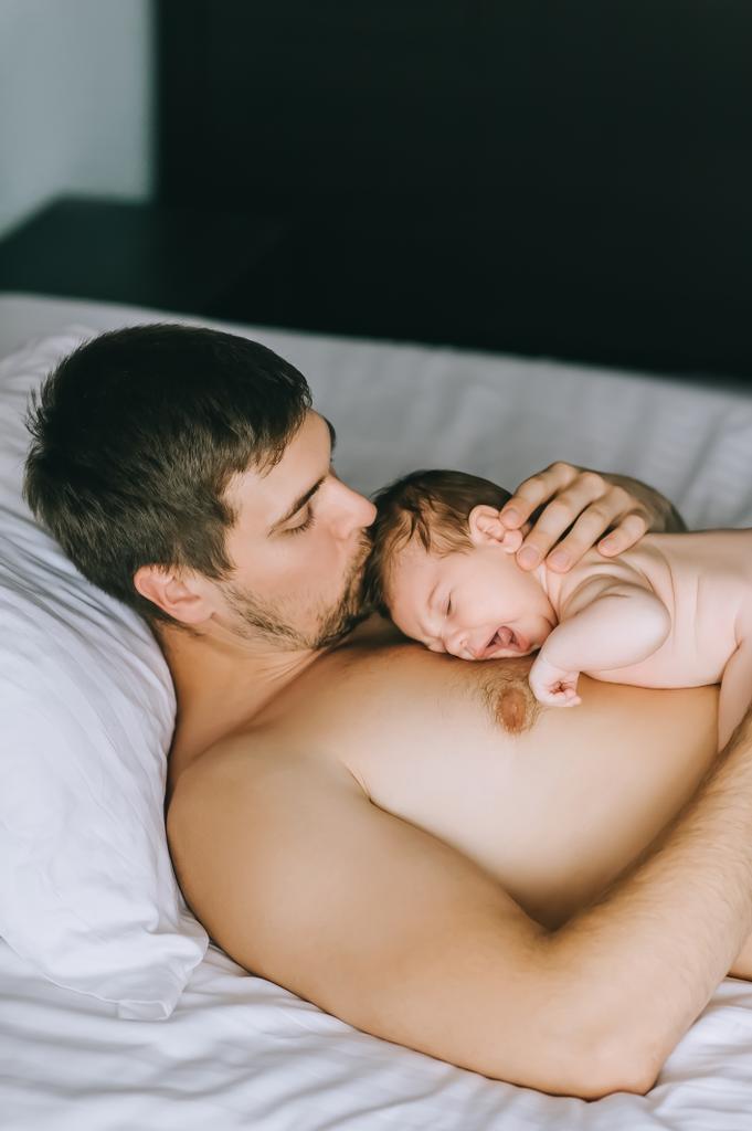 自宅のベッドで泣いている小さな赤ちゃんの息子をキスの父の高角度のビュー - 写真・画像