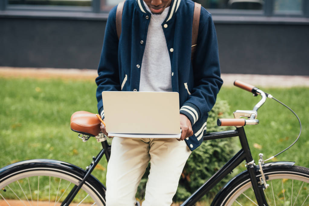vista cortada de freelancer elegante trabalhando com laptop enquanto se inclina na bicicleta
 - Foto, Imagem