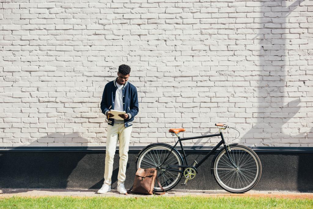 ドキュメントを読むと白いレンガの壁に自転車の近くに立ってアフリカ系アメリカ人のフリーランサー - 写真・画像