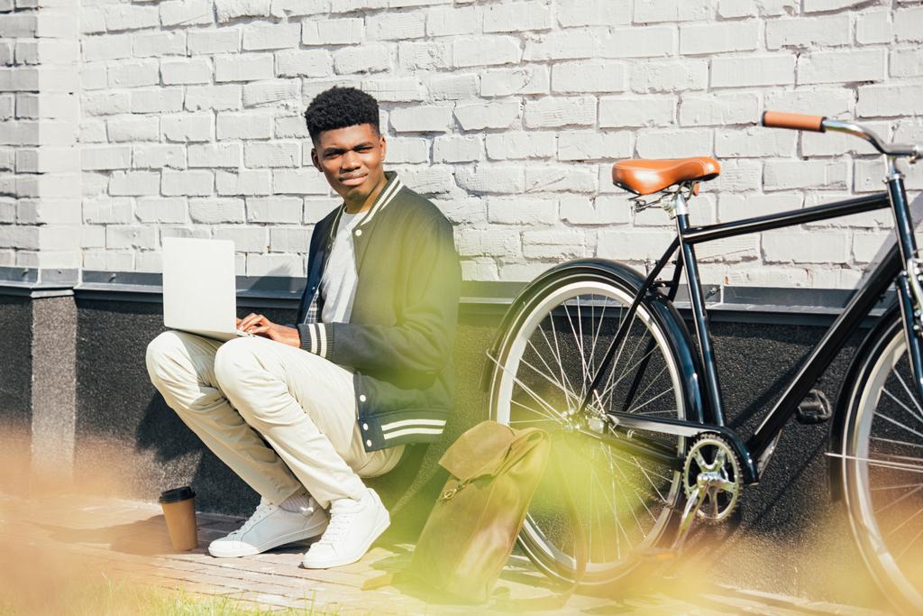 afro-amerikai teleworker használ laptop kerékpár közelében, a fehér téglafal - Fotó, kép