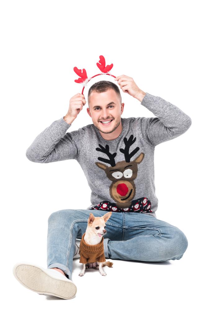 счастливый человек в положить праздничные рога оленя на голову с маленькой собачкой чихуахуа рядом изолированы на белом
 - Фото, изображение