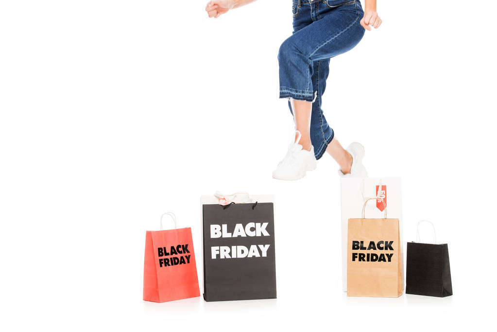 oříznutý pohled dívka, která skočila poblíž nákupní tašky s černý pátek prodej značek izolované na bílém - Fotografie, Obrázek